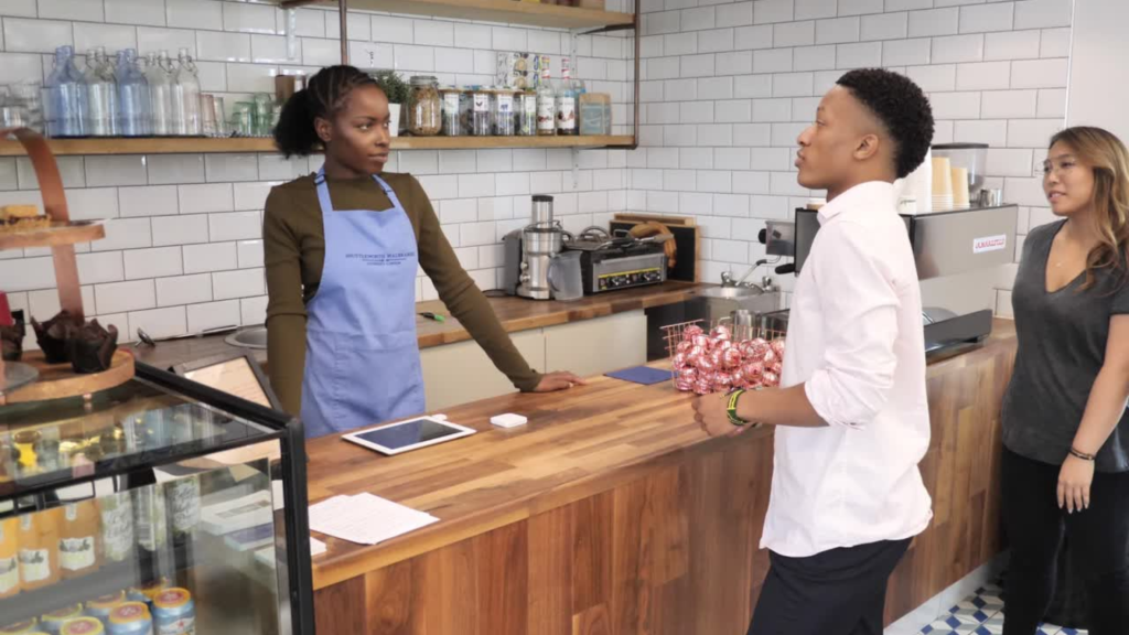 Small business owner at a café counter speaking with customers, representing strategies for how to get customers on Instagram.